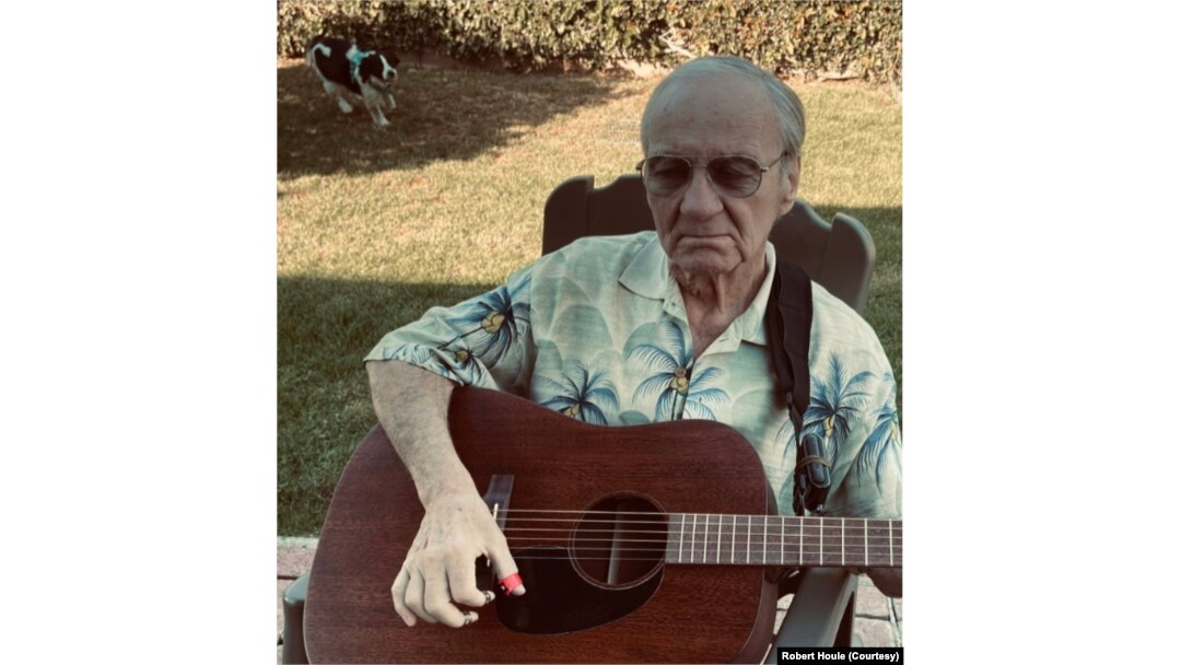 Bob plays his guitar in his backyard in Costa Mesa, California, as one of his Cocker Spaniels roams behind him.