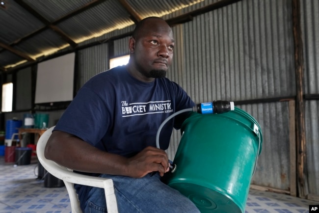 FILE - Derrick Mesulamu, the county director for the Bucket Ministry, a Christian nonprofit organization, demonstrates how to use a bucket filter to locals in Athi River, Machakos county, Kenya, Oct. 17, 2023.
