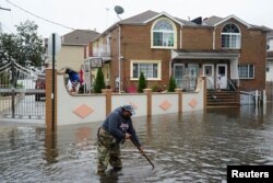 A resident attempts to unclog leaves and other debris from drainage holes in the Hamilton Beach neighborhood in the Queens borough of New York City, Sept. 29, 2023.