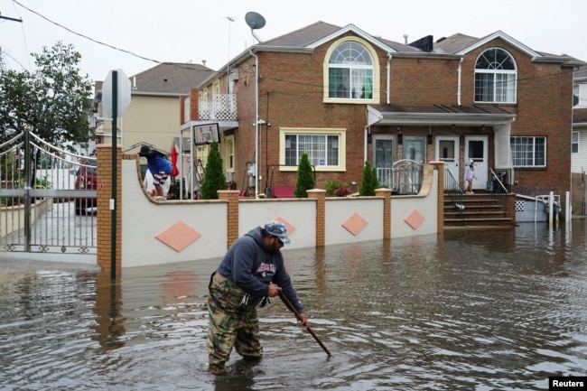 A resident attempts to unclog leaves and other debris from drainage holes in the Hamilton Beach neighborhood in the Queens borough of New York City, Sept. 29, 2023.