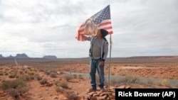 FILE - In this Oct. 25, 2018, photo, Brandon Nez displays his flag near his jewelry stand in Monument Valley, Utah. 