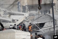 Emergency services work at a building hit by an air strike in Damascus, Syria, Jan. 20, 2024. Syrian and Iranian state media say an Israeli strike on t Damascus killed five Iranian advisers.