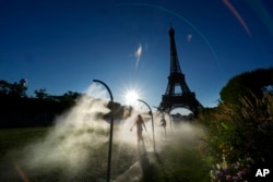 A spectator walks through a water mist sprayers on her way to Eiffel Tower Stadium to watch a beach volleyball at the 2024 Summer Olympics, July 28, 2024, in Paris, France.