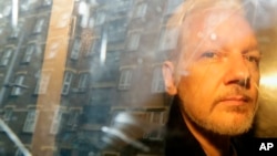 FILE - Buildings are reflected in the window as WikiLeaks founder Julian Assange is taken from court, where he appeared on charges of jumping British bail, in London, May 1, 2019.