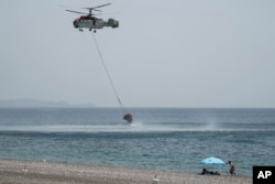 Ljudi posmatraju sa plaže dok vatrogasni helikopter uzima morsku vodu, tokom borbe protiv požara, nedaleko od sela Genadi, na ostrvu Rodos, južna Grčka, 27. jula 2023.