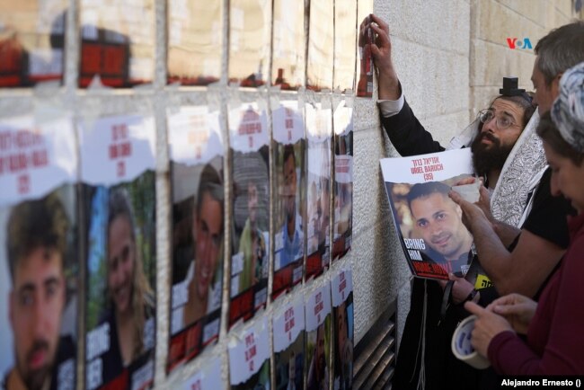 Varias personas colocan carteles con los rostros de los israelíes secuestrados por Hamás en el Muro de las Lamentaciones de Jerusalén.