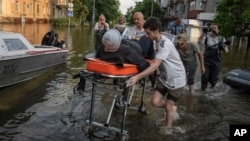 Volunteers transport a woman on a stretcher to be evacuated from a flooded neighborhood in Kherson, Ukraine, June 9, 2023.