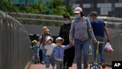 FILE - Women wearing face masks walk with masked children in Beijing, May 21, 2023.