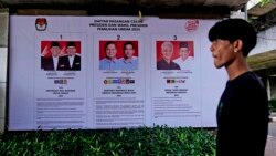 Seorang pria berjalan melewati spanduk Komisi Pemilihan Umum yang menampilkan foto-foto kandidat presiden di Jakarta, Senin, 22 Januari 2024. (Foto: AP)