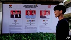 Seorang pria berjalan melewati spanduk Komisi Pemilihan Umum yang menampilkan foto-foto kandidat presiden di Jakarta, Senin, 22 Januari 2024. (Foto: AP)