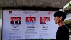 Seorang pria berjalan melintas di depan spanduk tiga calon presiden dan wakil presiden dalam pilpres 2024, di Jakarta, 22 Januari 2024. (Foto: Dita Alangkara/AP Photo)