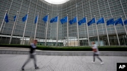 FILE - European Union flags wave in the wind as pedestrians walk by EU headquarters in Brussels, Sept. 20, 2023. 