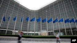 FILE - European Union flags wave in the wind as pedestrians walk by EU headquarters in Brussels, Sept. 20, 2023. 