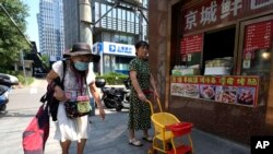 An elderly woman walks by a store selling snacks in Beijing, July 17, 2023. 