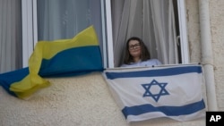 Tatyana Prima, who fled Mariupol, Ukraine, poses for a portrait with her national flag and the Israeli flag she displays outside of her apartment window in Ashkelon, southern Israel, Wednesday, Nov. 8, 2023. (AP Photo/Maya Alleruzzo)