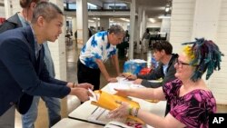 El presidente interino del Partido Demócrata de Hawái, Adrian Tam, coloca su boleta del caucus presidencial para su recuento en un sobre que tiene la voluntaria del partido Bonnie Fraser en Honolulu el miércoles 6 de marzo de 2024. (Foto AP/Audrey McAvoy)