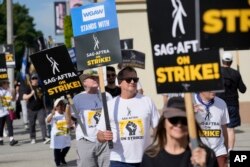 WGA and SAG-AFTRA member Michael Hitchcock, center, carries a sign on the picket line outside Paramount Pictures studio in Los Angeles, Sept. 27, 2023. Hollywood's writers strike was declared over Tuesday night, but the actors strike continues.