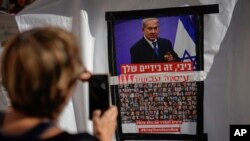 Seorang perempuan mengabadikan poster dengan foto orang-orang yang disandera Hamas dan foto Perdana Menteri Israel Benjamin Netanyahu, di Tel Aviv, Israel, Selasa, 21 November 2023. (Foto: Ariel Schalit/AP Photo)