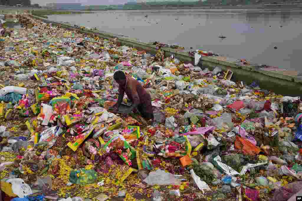 Seorang pria mencari bahan yang dapat didaur ulang di tengah persembahan (sesaji) dan patung dewi Hindu Dashama yang ditinggalkan olah ummat Hindu di tepi Sungai Sabarmati setelah berakhirnya festival Dashama yang berlangsung selama 10 hari di Ahmedabad, India. (AP)