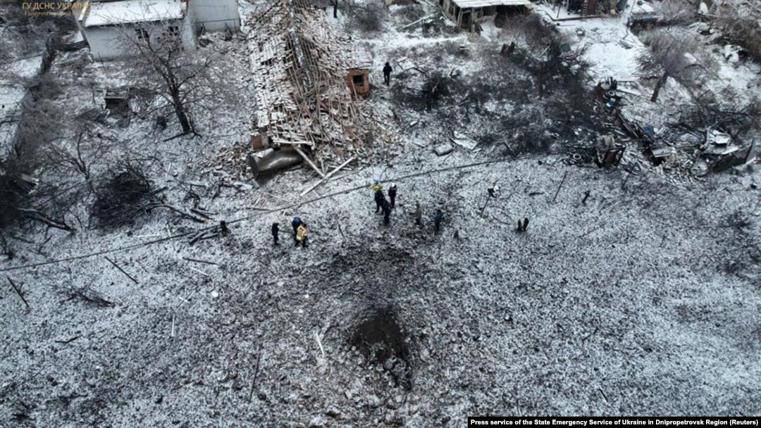 People stand next to a destroyed residential house and a crater at the site of a Russian missile strike in Dnipropetrovsk Region, Ukraine, Jan. 8, 2024. 