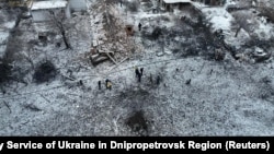 People stand next to a destroyed residential house and a crater at the site of a Russian missile strike in Dnipropetrovsk Region, Ukraine, Jan. 8, 2024. 