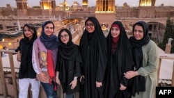 Women pose for a group photo with wind catchers ("badir" in Persian) dotting the skyline behind, on a rooftop in Iran's central city of Yazd on July 3, 2023.