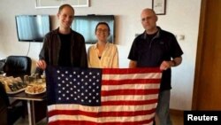 Evan Gershkovich, Alsu Kurmasheva, dan Paul Whelan, yang ditahan di Rusia, berpose dengan bendera AS saat merayakan kebebasan mereka dalam foto selebaran tanpa tanggal yang diperoleh pada 1 Agustus 2024. (Pemerintah AS/Handout via Reuters)