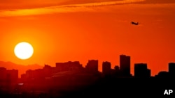A jet takes flight from Sky Harbor International Airport as the sun sets over downtown Phoenix, July 12, 2023.