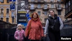 (FILE) Women and a child walk near a recruitment poster for the Azov Assault Brigade of the National Guard of Ukraine, amid Russia's attack on Ukraine, in Kyiv, Ukraine, November 8, 2023.