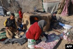 Seorang perempuan Palestina dan anak-anak pengungsi yang melarikan diri dari Khan Yunis, memasak roti di Rafah, lebih jauh ke selatan dekat perbatasan Jalur Gaza dengan Mesir, pada 6 Desember 2023. (MOHAMMED ABED / AFP)