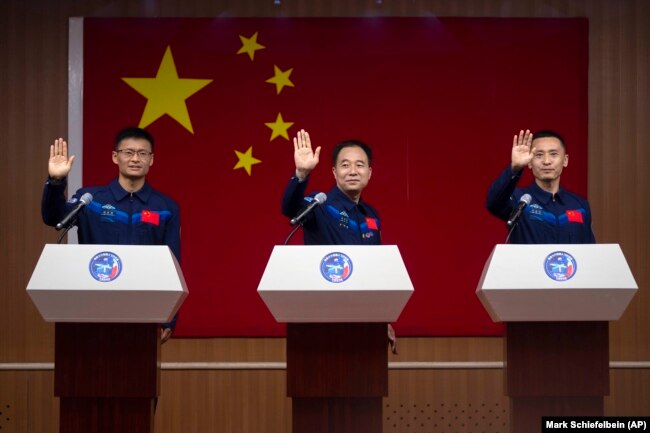 Chinese astronauts for the upcoming Shenzhou-16 mission, from left, Gui Haichao, Jing Haipeng, and Zhu Yangzhu wave as they stand behind glass during a meeting with the press at the Jiuquan Satellite Launch Center in northwest China on Monday, May 29, 2023. China's space program plans to land astronauts on the moon before 2030, a top official with the country's space program said Monday. (AP Photo/Mark Schiefelbein)