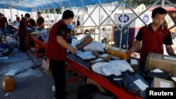 FILE - Delivery workers sort packages on a conveyor belt, ahead of a shopping festival at a logistics station in Beijing, June 12, 2023. 