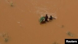 People hold on to plants as they wade through flood waters after they were displaced following heavy rains in Garsen, Tana Delta, Kenya, Nov. 23, 2023. 