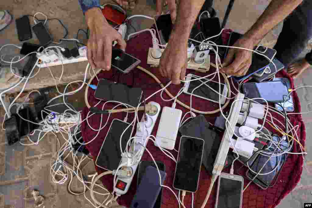 People sit by phone chargers connected to a communal group of electric socket hubs outside a closed pharmacy in Rafah in the southern Gaza Strip, amid ongoing battles between Israel and the Palestinian Hamas movement.&nbsp;(Photo by Mohammed ABED / AFP)