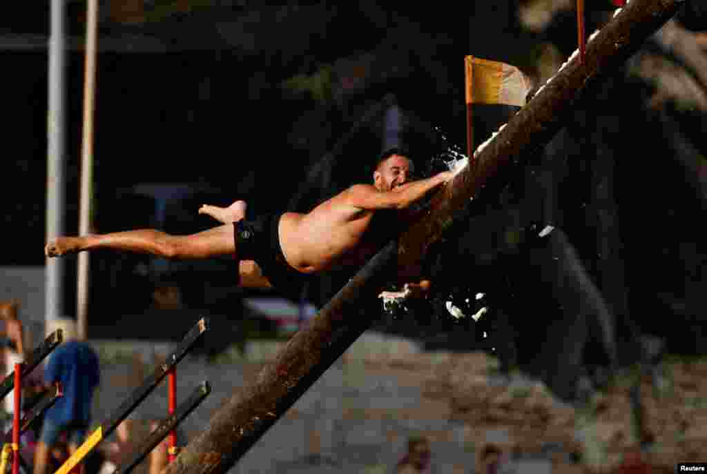 A competitor tries to grab a flag as he falls off the "gostra", a pole covered in lard, during the celebrations of the religious feast of St. Julian, patron of the town of St. Julian's, Malta, Aug. 18, 2024.