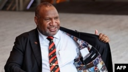 Perdana Menteri Papua Nugini James Marape memperlihatkan bagian dalam jaketnya yang dipenuhi foto-foto lama dirinya, saat wawancara di Sydney pada 11 Desember 2023. (Foto: AFP)