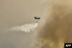 Helikopter Chinook militer terbang di atas wilayah Magoula, 25 km barat daya Athena pada 18 Juli 2023, tempat kebakaran hutan terjadi. Eropa bersiap menghadapi suhu tinggi baru pada 18 Juli 2023, di bawah gelombang panas tanpa henti dan kebakaran hutan yang menghanguskan sebagian belahan bumi utara. (Foto: AFP)