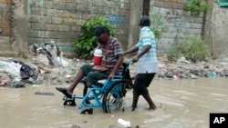 Un hombre en silla de ruedas es ayudado a atravesar una calle inundada después de una fuerte lluvia, en Puerto Príncipe, Haití, el sábado 3 de junio de 2023.