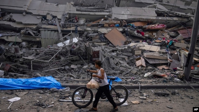 A Palestinian child walks with a bicycle by the rubble of a building after it was hit by an Israeli airstrike, in Gaza City, Oct. 8, 2023.