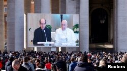 Monsignor Paolo Braida reads next to Pope Francis as they appear on a screen in St. Peter's Square, during the Angelus prayer led by Pope Francis from Santa Marta chapel at the Vatican, Nov. 26, 2023. 