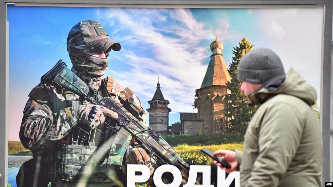 Seorang pria berjalan melewati poster prajurit Rusia bertuliskan "Tanah Air yang kami pertahankan" di pameran jalanan poster bertema militer di pusat Saint Petersburg, 17 Februari 2023. (Olga MALTSEVA / AFP)