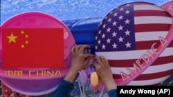 Un comerciante ata unas flores decoragivas entre dos banderas de China y Estados Unidos con forma de planeta, en una tienda durante el Carnaval de Primavera en Beijing, el 13 de mayo de 2023.