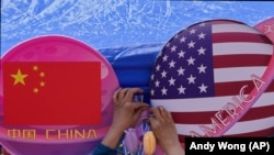 A vendor tights a flowers deco in between of the planets shaped of China and American flags on display at a store during a Spring Carnival in Beijing on May 13, 2023. (AP Photo/Andy Wong)