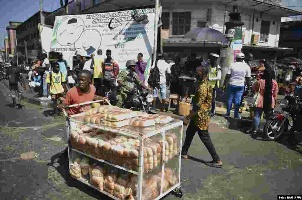 Um membro das Forças Armadas da Serra Leoa passa por um vendedor ambulante em Freetown, a 27 de novembro de 2023, após confrontos que abalaram a capital da Serra Leoa, Freetown, a 26 de novembro de 2023. (Foto por Saidu BAH / AFP)