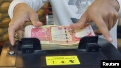 (FILE) A man counts Iraqi dinars on a money counting machine in Iraq.