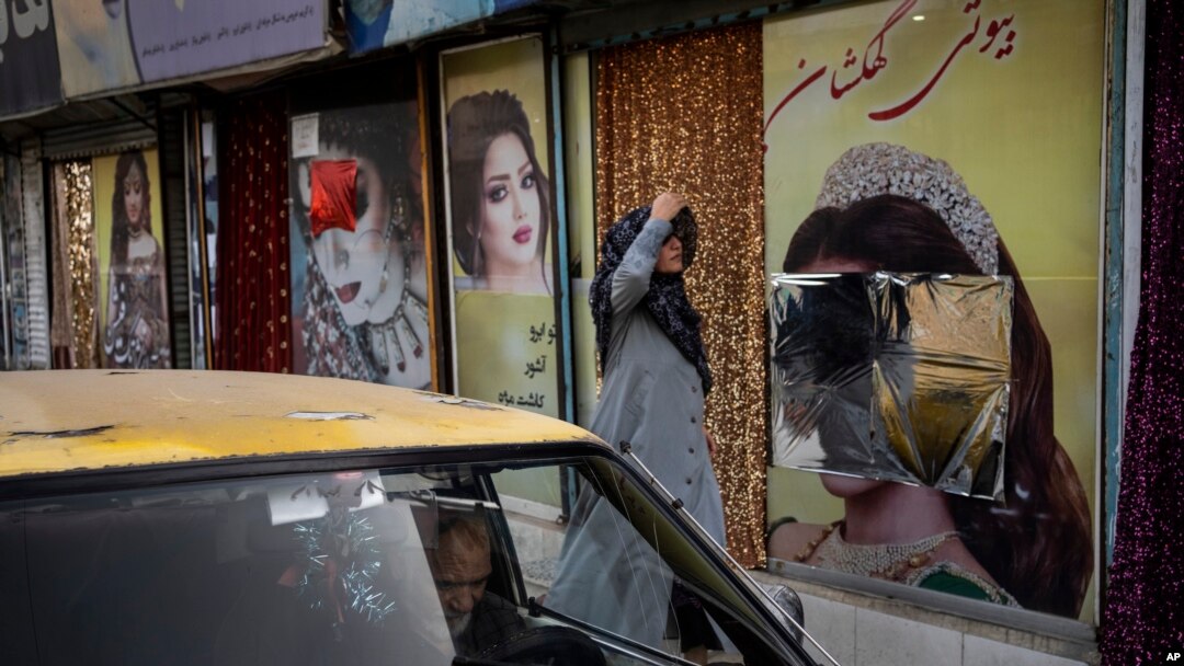 FILE - A woman walks past a beauty salon with its window decorations partially covered up, in Kabul, Afghanistan, Sept. 12, 2021.