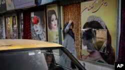 FILE - A woman walks past a beauty salon with its window decorations partially covered up, in Kabul, Afghanistan, Sept. 12, 2021.