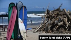 Seorang turis bersiap untuk berselancar di Pantai Kuta di Denpasar, Bali, pada 16 April 2023. Seorang peselancar Australia yang dipenjara karena telanjang dan menyerang beberapa orang saat mabuk di Aceh akan dideportasi ke negaranya. (Foto: Sonny Tumbelaka/AFP)