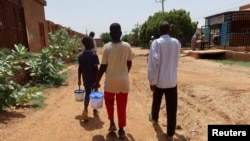 FILE - People hold containers filled with food distributed by volunteers in Omdurman, Sudan, Sept. 3, 2023.