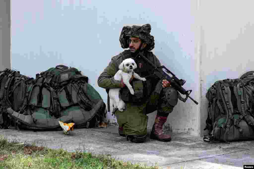 An Israeli soldier holds a rescued dog as he takes position near a bomb shelter in Kibbutz Kfar Aza, in southern Israel.